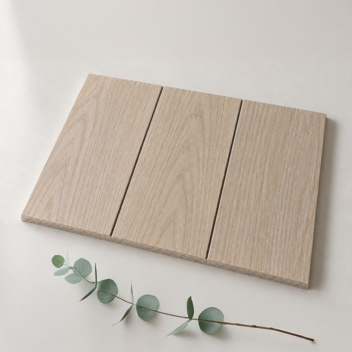 Three rectangular light oak wood panels arranged side by side on a white surface, with a small eucalyptus sprig placed below them.